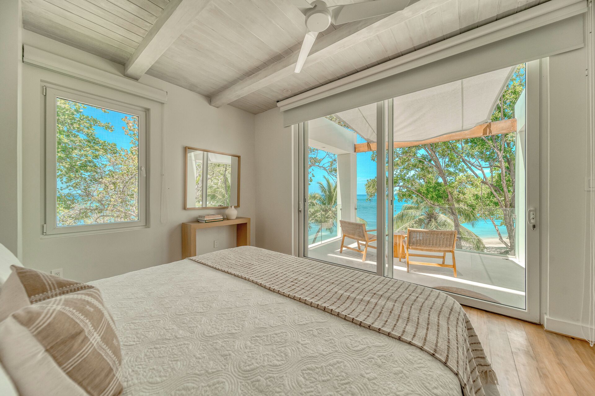A bedroom with a large bed, a nightstand, a mirror, and a view of the ocean through sliding glass doors.