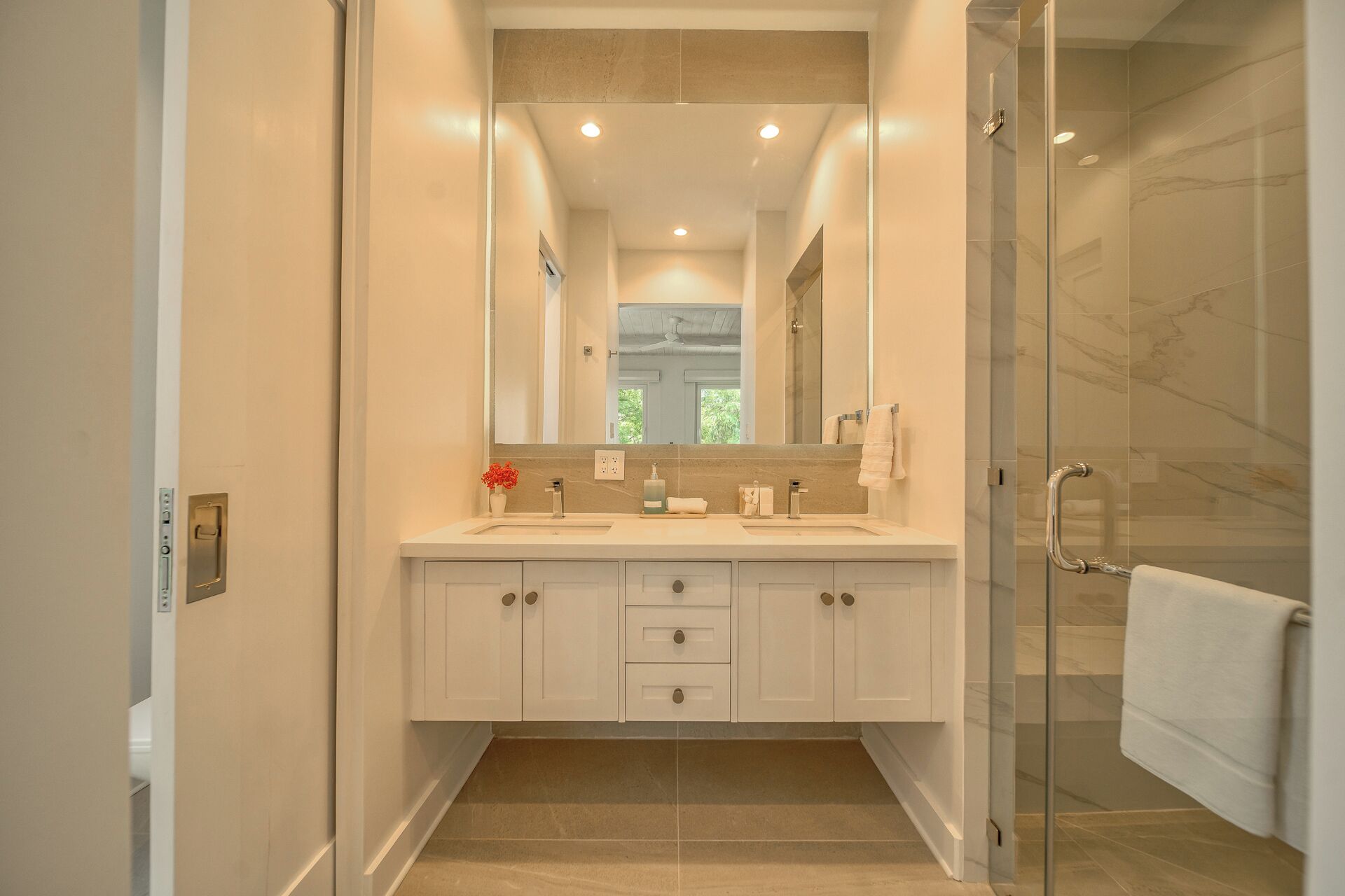 A modern bathroom with a glass shower enclosure, a large mirror, and a white vanity with multiple drawers.