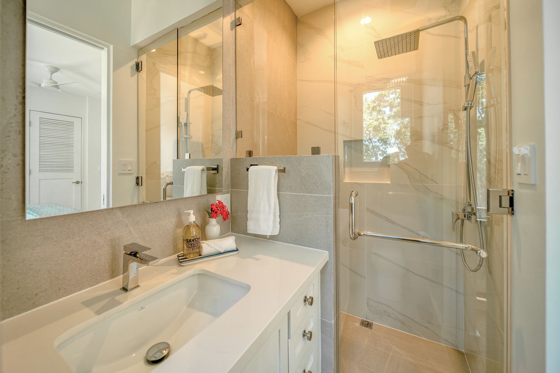 Une salle de bain moderne avec une douche à parois de verre, un grand miroir et un lavabo blanc.