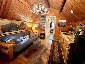 L’intérieur d’un chalet confortable en bois, avec un canapé, un lustre, une cheminée et un coin cuisine.