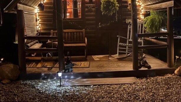 En stuga av trä med en veranda, en bänk och en välkomstskylt.