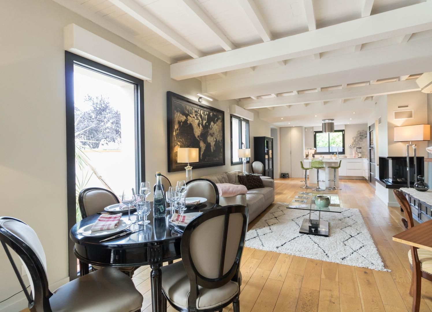 A modern living room with a dining area, kitchen, and a large window offering a view.