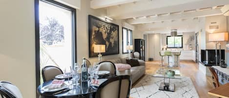 A modern living room with a dining area, kitchen, and a large window offering a view.