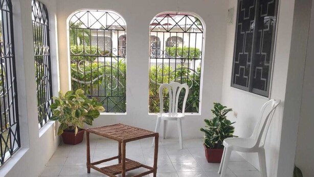 Een klein, afgesloten balkon met een betegelde vloer, een houten tafel, twee witte plastic stoelen en potplanten.