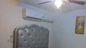 Een slaapkamer met een gestoffeerd hoofdeinde, een bed met een bloemenbedekker, een plafondventilator en een airconditioningsysteem.