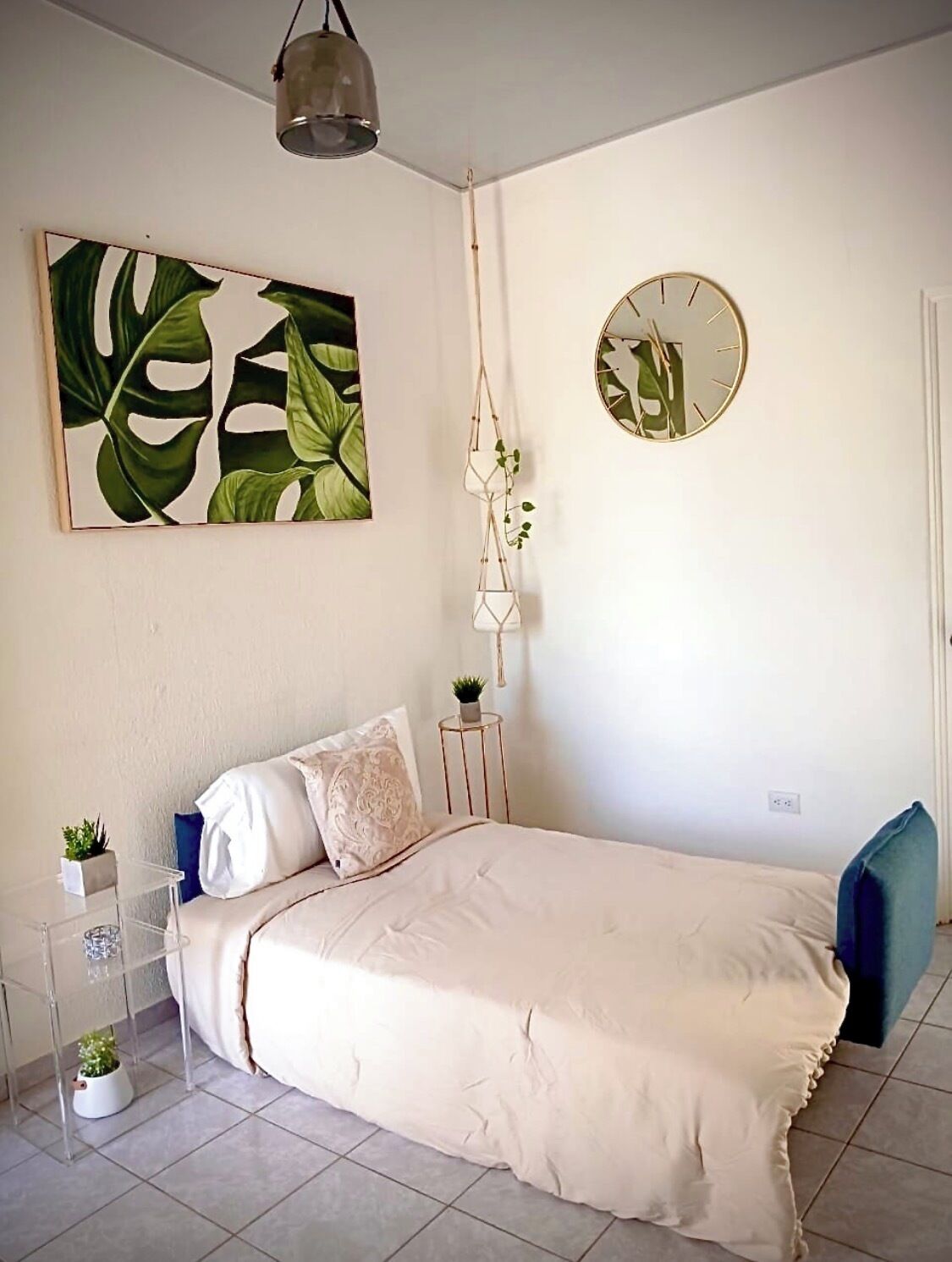 A bedroom with a bed, a wall clock, a plant, and a framed artwork.