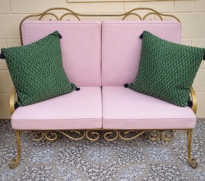 A pink sofa with green pillows against a beige wall, placed on a patterned tile floor.