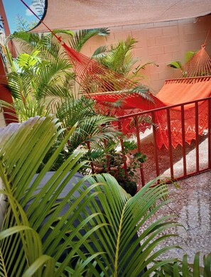 Un balcón con vista a una pared de ladrillo, rodeado de exuberantes plantas verdes y una hamaca roja.