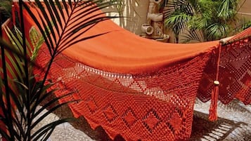 Un hamac avec un auvent rouge, installé dans une cour dont le sol est recouvert de carreaux et où l’on trouve des plantes en pot.