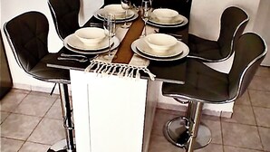Uma mesa de jantar com quatro cadeiras, um console branco central e um chão ladrilhado.