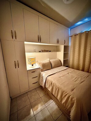 Une chambre à coucher comprenant un lit, une table de chevet, une étagère avec des objets décoratifs et une armoire.