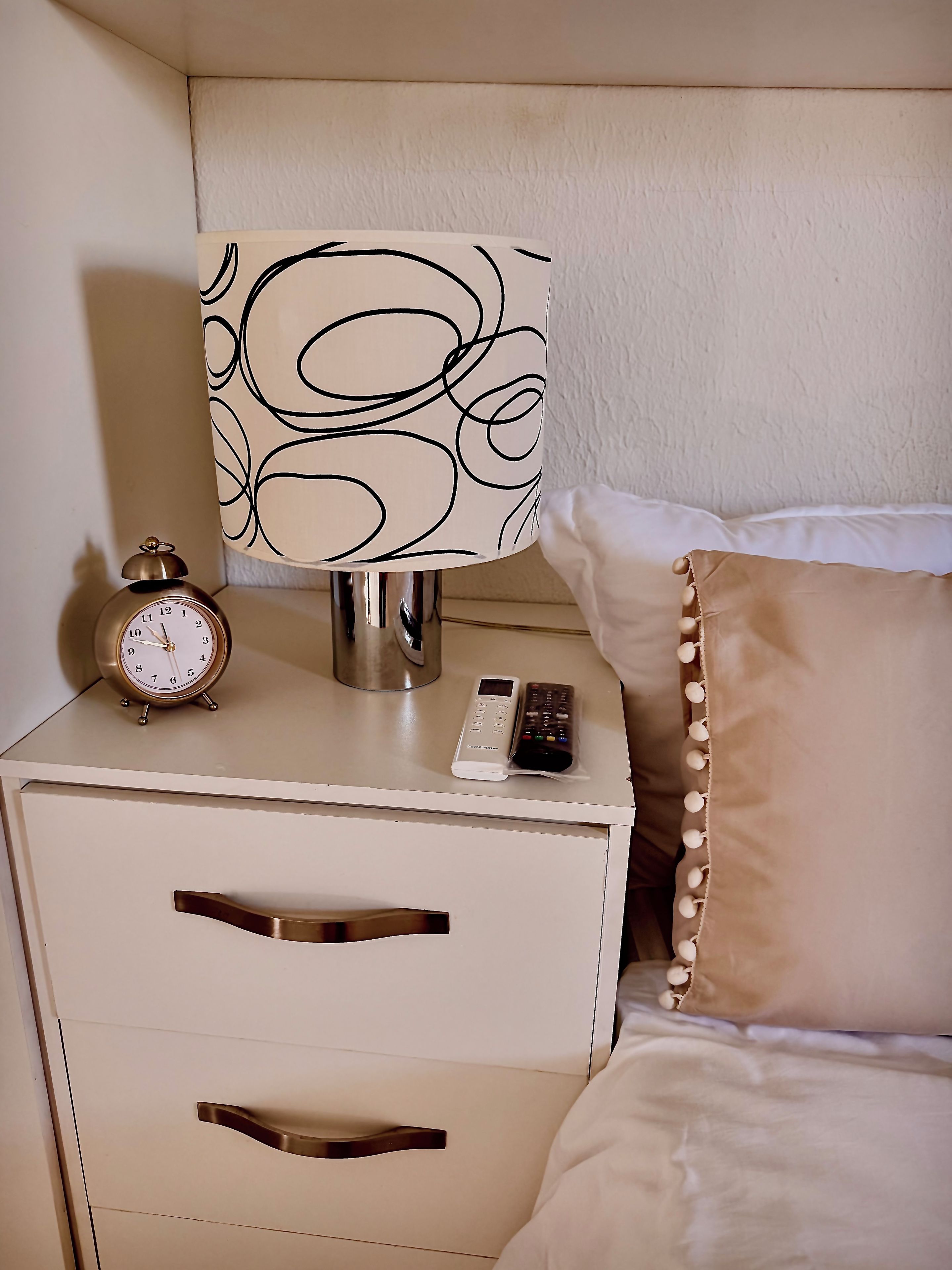 A bedside table with a lamp, a clock, and a remote control.