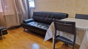 Una habitación con un sofá de cuero, una mesa de comedor con una silla y un taburete pequeño.