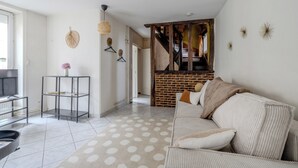 A modern living room with a sofa, a coffee table, and a TV. There is a staircase leading to a loft area.