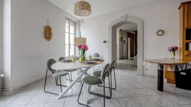 A dining area with a white table, grey chairs, and a woven pendant light.