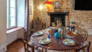 Un comedor con pared de piedra, chimenea y mesa preparada para una comida.