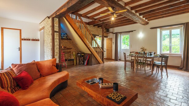 Amplia sala de estar con escalera de madera, una mesa de comedor con sillas y un sofá con cojines rojos.