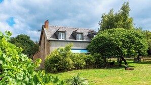 Una casa con techo inclinado, una chimenea visible y una piscina al fondo.