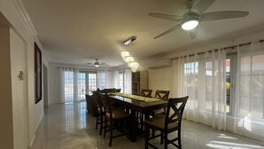 A spacious dining area with a long table, chairs, ceiling fans, and large windows. - Ocean View Villa Tree House @ Little Bay (Hanover Parish)