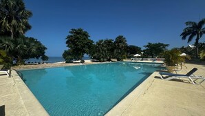 A rectangular swimming pool with clear blue water, surrounded by a sandy area and palm trees. - Ocean View Villa Tree House @ Little Bay (Hanover Parish)