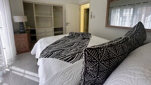 A bedroom with two beds, a wardrobe, a bedside table, and a window with curtains. - Ocean View Villa Tree House @ Little Bay (Hanover Parish)