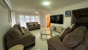 A living room with two sofas, a coffee table, a TV, and a ceiling fan. - Ocean View Villa Tree House @ Little Bay (Hanover Parish)