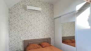 Un dormitorio con cama, un mueble negro de almacenaje, un armario y un techo con vigas de madera a la vista.