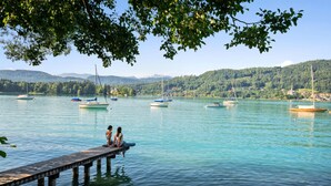 A calm lake with boats, a wooden pier, and a forested hillside in the background. - Gorgeous apartment in Pörtschach am Wörtherse with lake view (Pörtschach am Wörtherse)