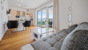 A modern apartment with a living room, kitchen, and dining area. There is a large window providing a view of the outdoors. - Gorgeous apartment in Pörtschach am Wörtherse with lake view (Pörtschach am Wörtherse)