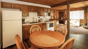 A wooden kitchen with a dining table and chairs, a refrigerator, stove, and cabinets. - Cubs Nest (Sugarloaf)