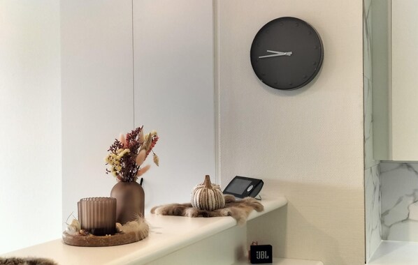 A modern interior with a round wall clock, a tablet on a shelf, and a decorative arrangement including a vase and a small pumpkin.