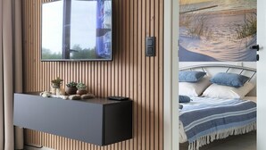 Ein Schlafzimmer mit einem Bett, einem Nachttisch, einem an einer Holzwand montierten Fernseher und einem Gemälde, das eine Strandansicht zeigt.