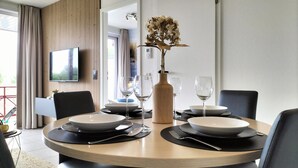 Ein moderner Essbereich mit einem runden Tisch für zwei Personen, einer Vase mit Trockenblumen und einem an der Wand befestigten Fernseher.