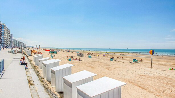 Ein Strand mit temporären Strukturen, einem klaren Himmel und einem weiten Blick auf das Meer.