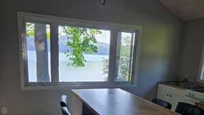 Une cuisine dotée d’un grand îlot central, de tabourets de bar et offrant une vue sur un lac grâce à de grandes fenêtres.
