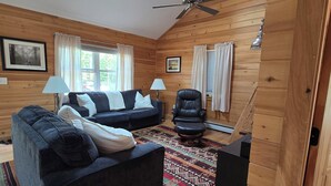 A cozy wooden interior with a sofa, armchairs, and a ceiling fan.
