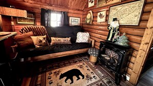 A log cabin interior with a sofa, fireplace, and various wall decorations. - The Raven tiny log cabin in The Forest (Cosby)