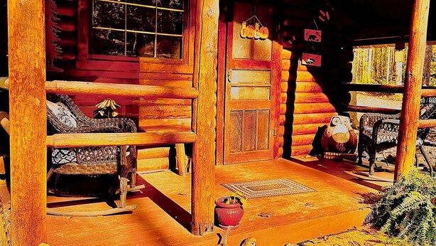 A log cabin with a porch, a rocking chair, a fireplace, and a window. - The Raven tiny log cabin in The Forest (Cosby)