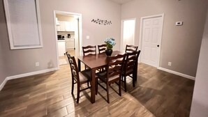 A dining room with a wooden table and chairs, a vase with flowers, and a kitchen in the background. - Comfy 4-bedroom house in Mount Clemens (Mount Clemens)