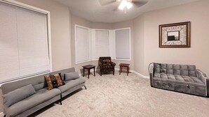 A living room with a grey sofa, a patterned armchair, two small tables, and a grey sofa with a curved backrest. - Comfy 4-bedroom house in Mount Clemens (Mount Clemens)