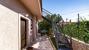 A narrow pathway leading to a building with a metal staircase and a door.