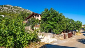 A residential area with a two-story house, a stone wall, and a clear blue sky.