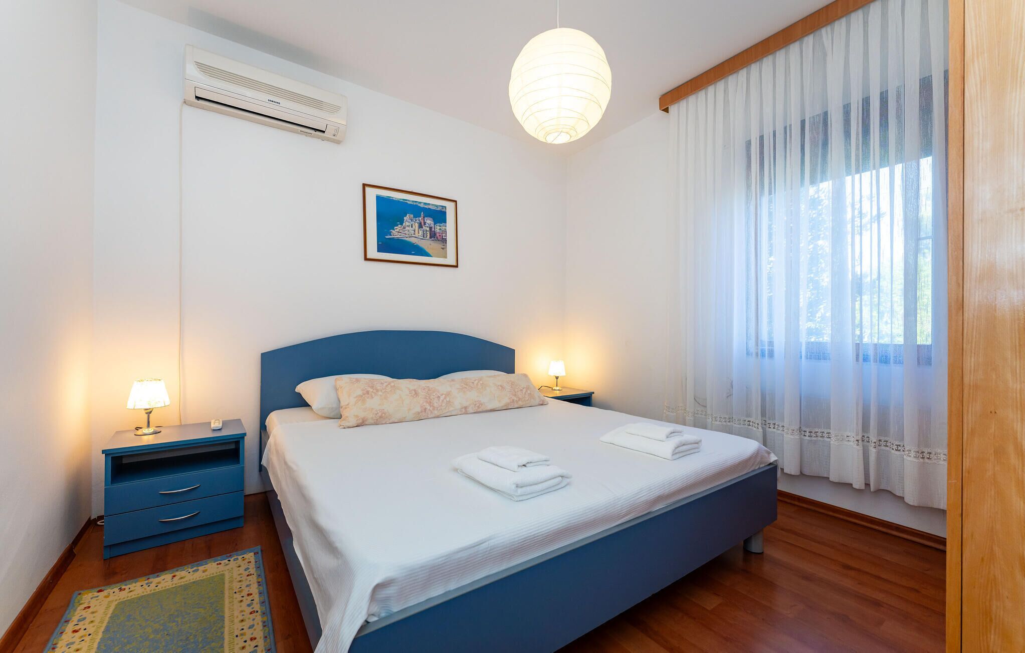 A bedroom with a bed, bedside lamps, a picture on the wall, and a window with curtains.