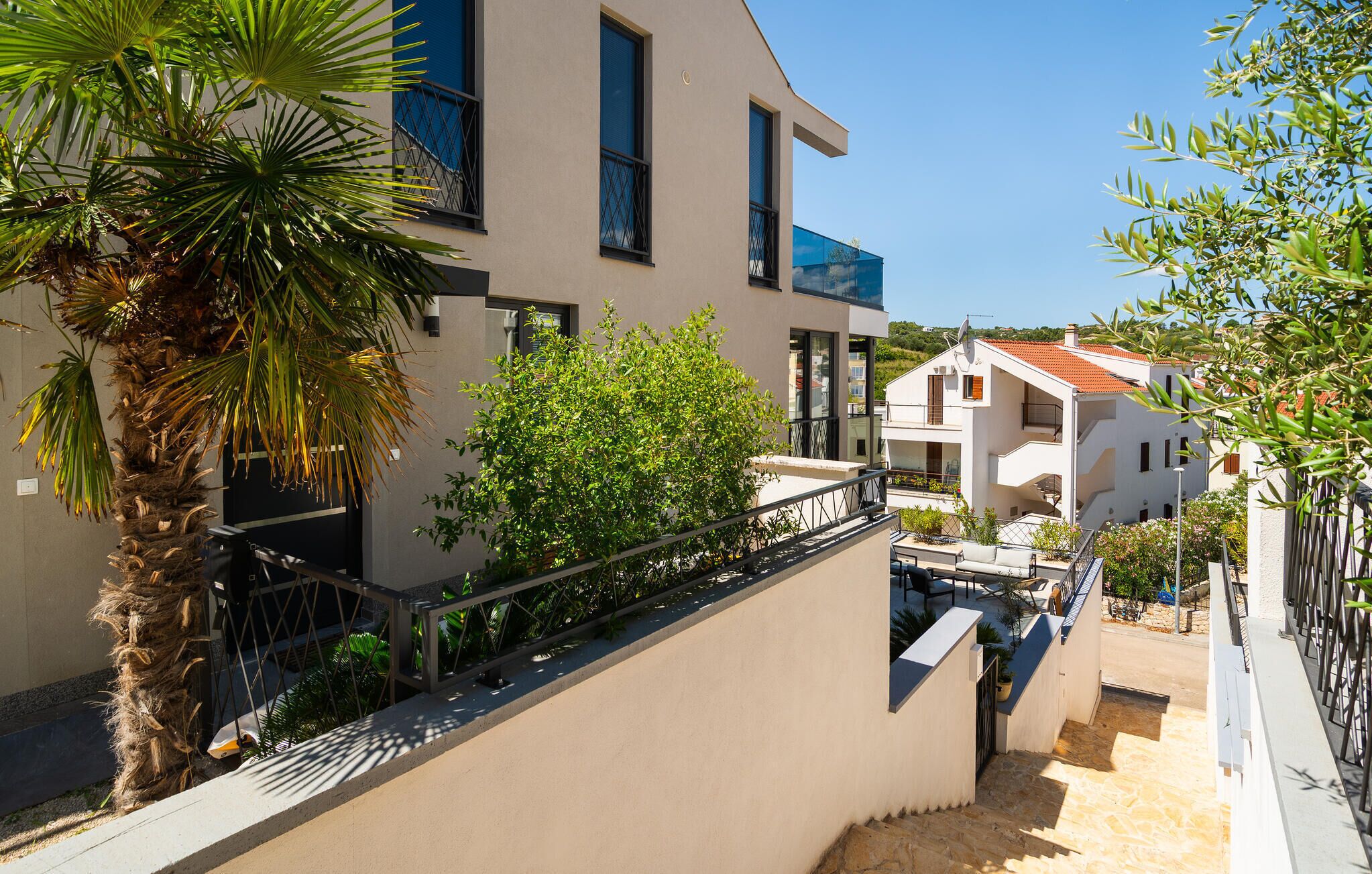 Un bâtiment moderne à deux étages, doté de balcons, d’un palmier et surplombant un ciel bleu azur.