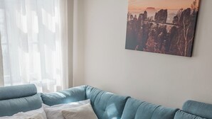 A modern living room with a blue sofa, a white throw blanket, and a painting on the wall. - Apartment Flurin in the heart of Königstein with parking lot. Family friendly (Königstein)