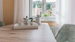 A dining table with a tray of cups and a kettle, a window with a view of buildings, and a chair with a striped cushion. - Apartment Flurin in the heart of Königstein with parking lot. Family friendly (Königstein)