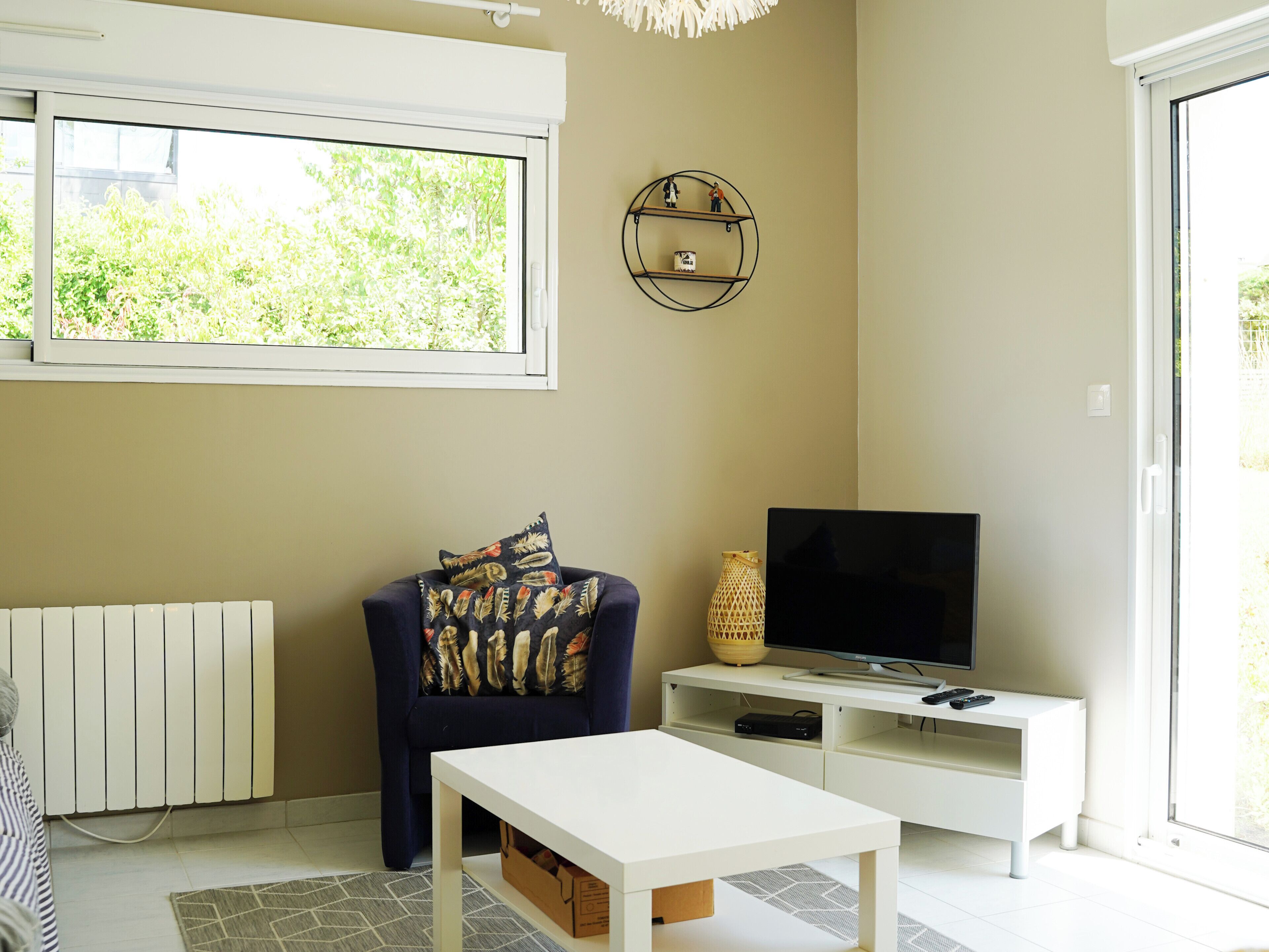 A living room with a sofa, a TV on a stand, a white coffee table, and a window with a view of greenery.