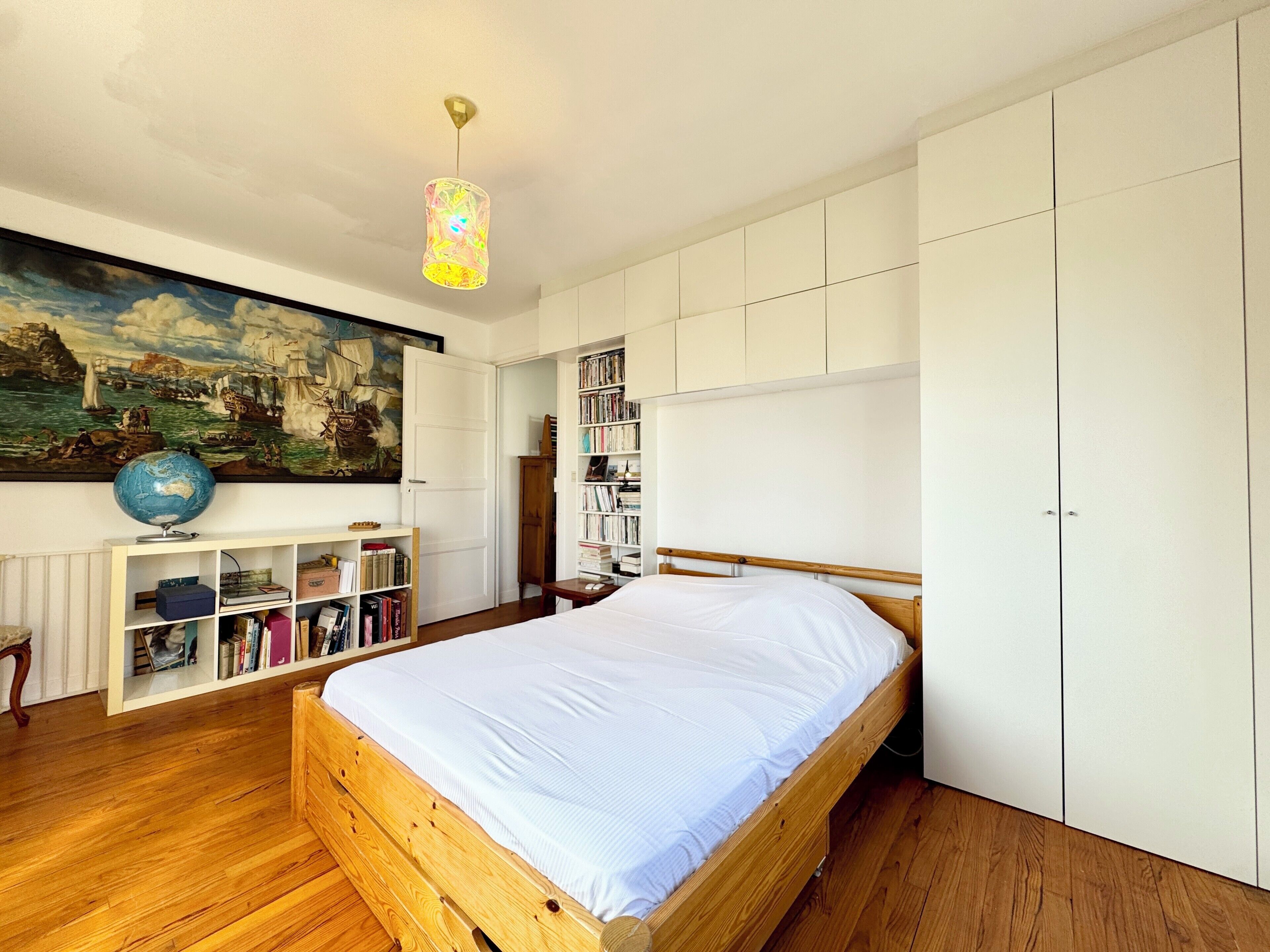 Une chambre à coucher avec un lit en bois, une armoire blanche, des étagères, un globe terrestre et un tableau sur le thème de la mer.