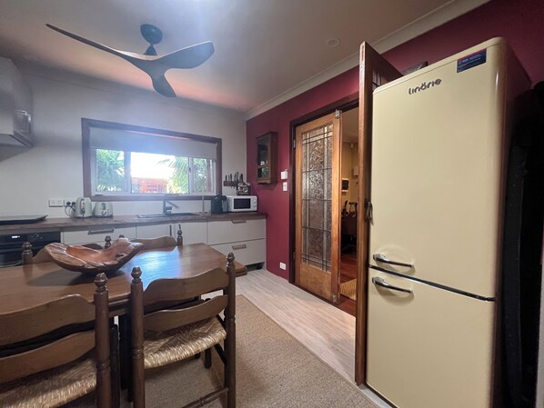 A kitchen with a dining table, chairs, a microwave, a refrigerator, and a window with a view of greenery.
