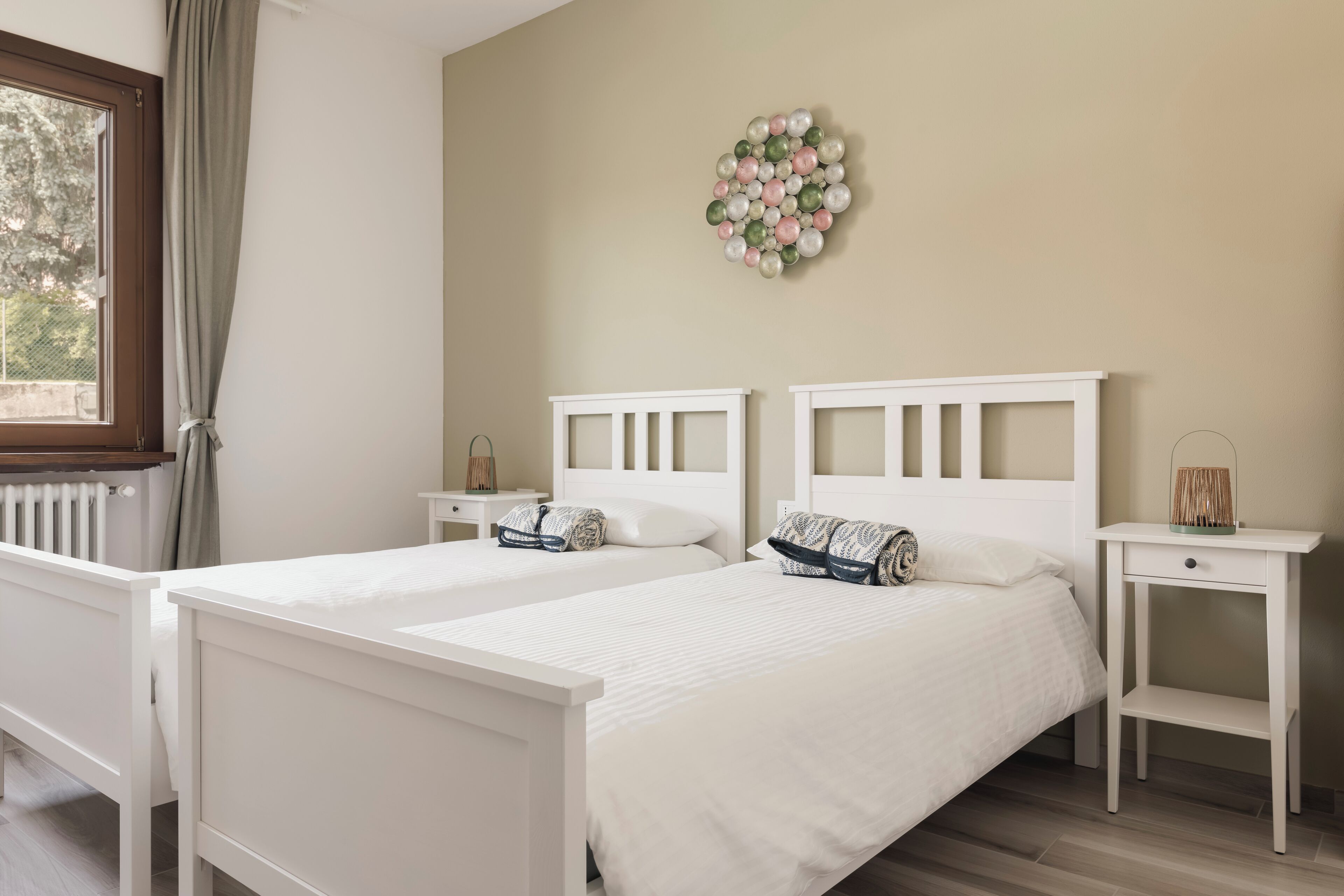 A bedroom with two white beds, a bedside table with a lamp, and a wall decoration.